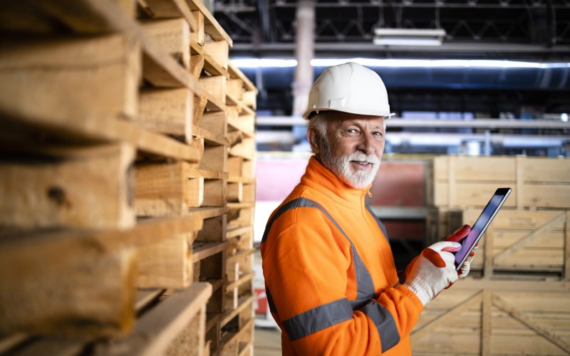 Warehouse worker in safety equipment and hard hat holding tablet computer and managing goods dispatching.